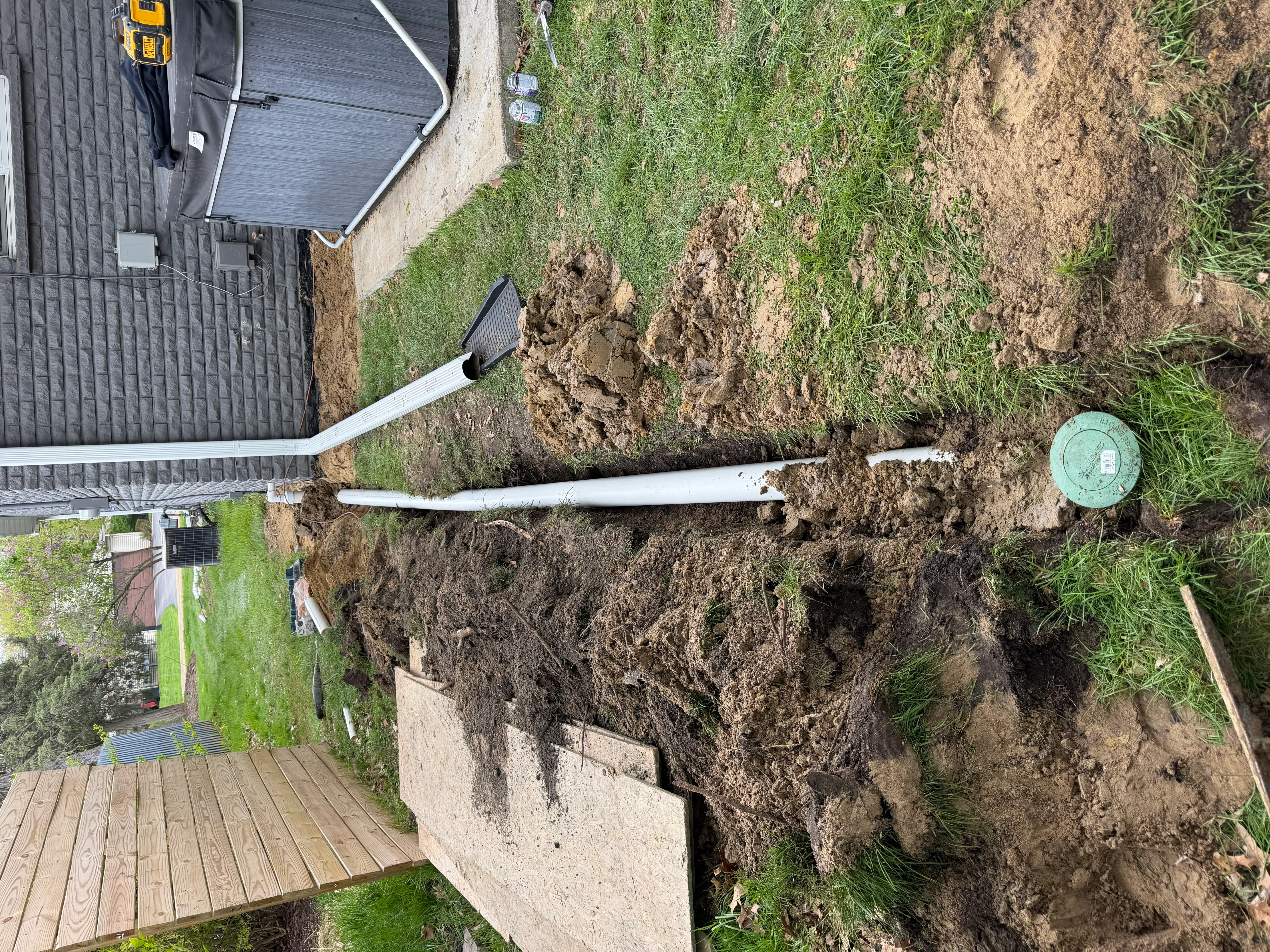 Exterior foundation drainage pipe installation with sump basin and excavated soil around home foundation