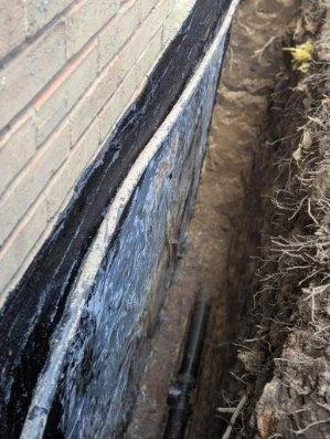 Black waterproofing membrane applied to exterior foundation wall with graded soil