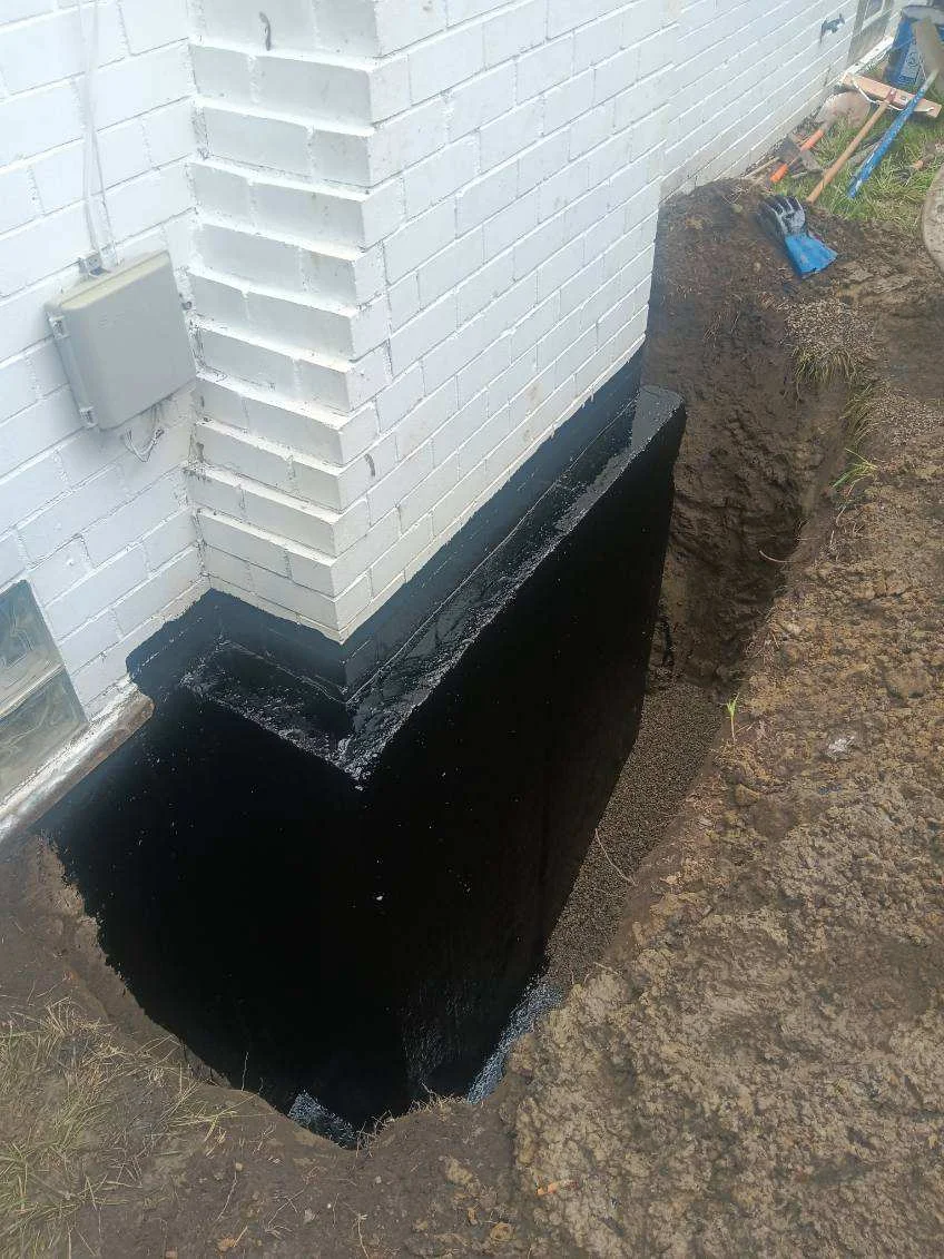 Black waterproof membrane applied to white brick foundation with excavated soil grading