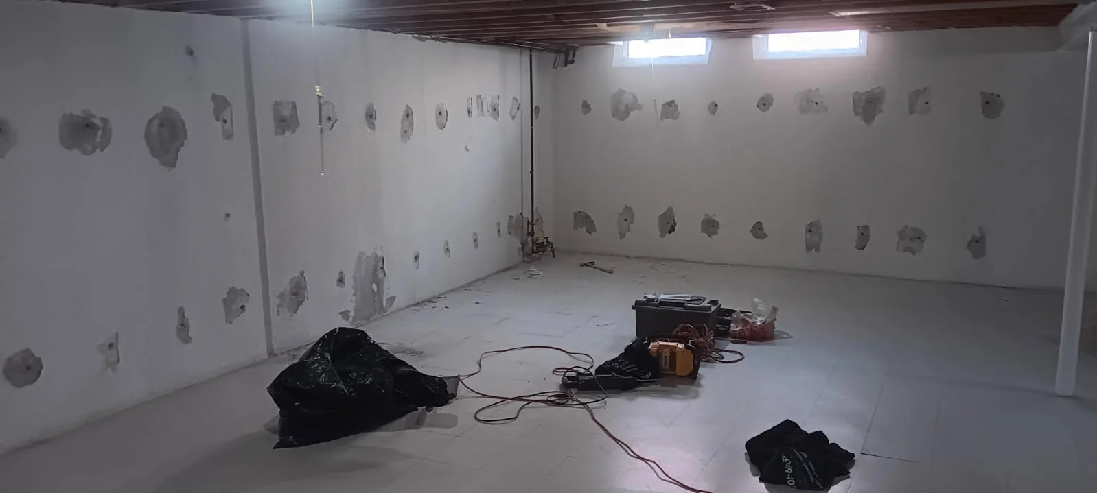 Basement interior with white drywall and multiple crack injection ports installed on foundation walls