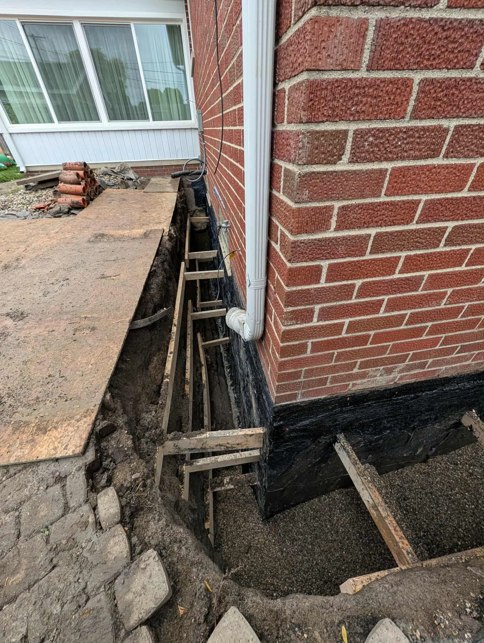 Exposed foundation trench with new drainage tile and waterproofing membrane installed along brick foundation wall