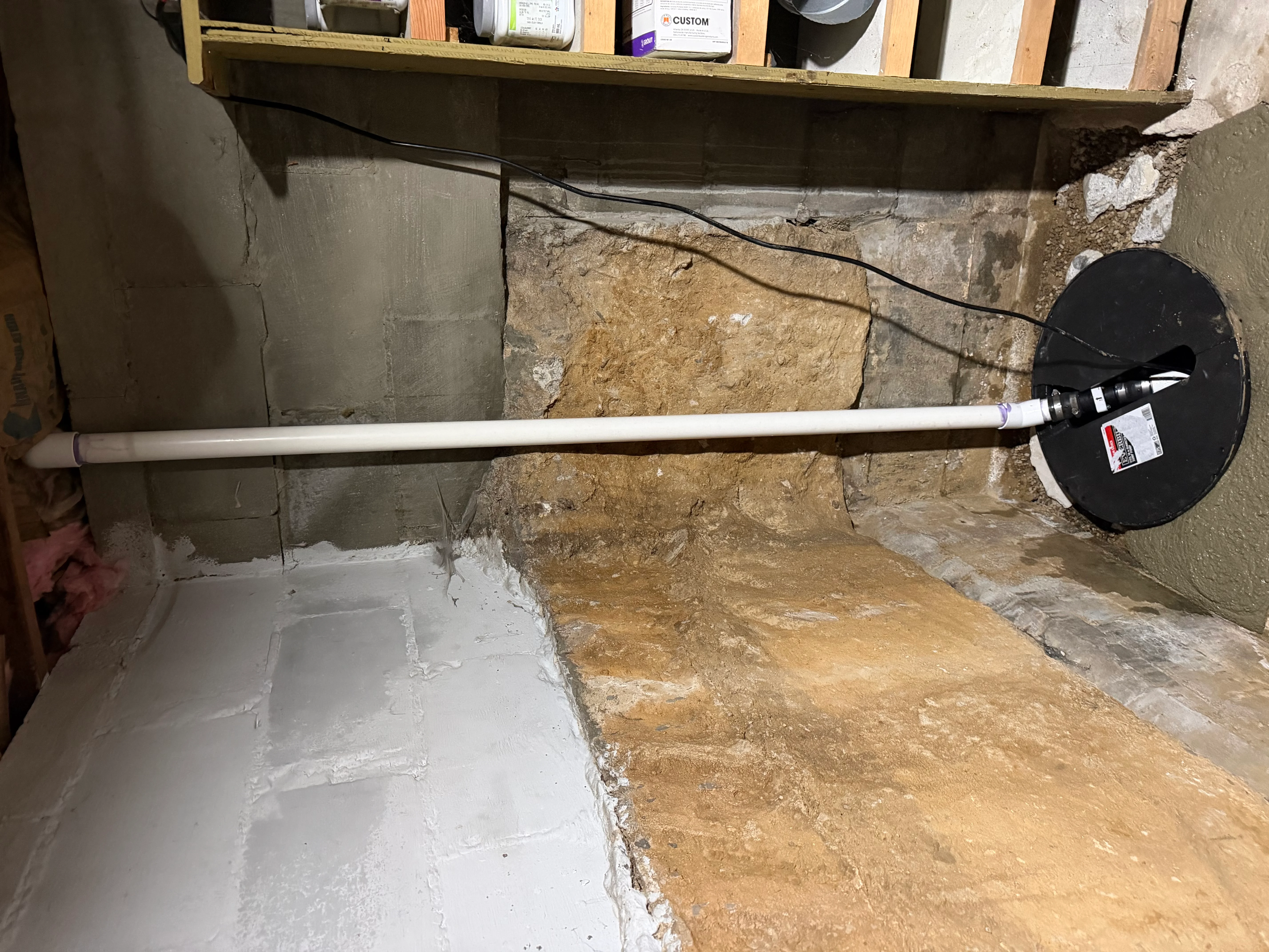 Interior basement waterproofing with white membrane, drainage pipe, and collection basin against concrete foundation wall