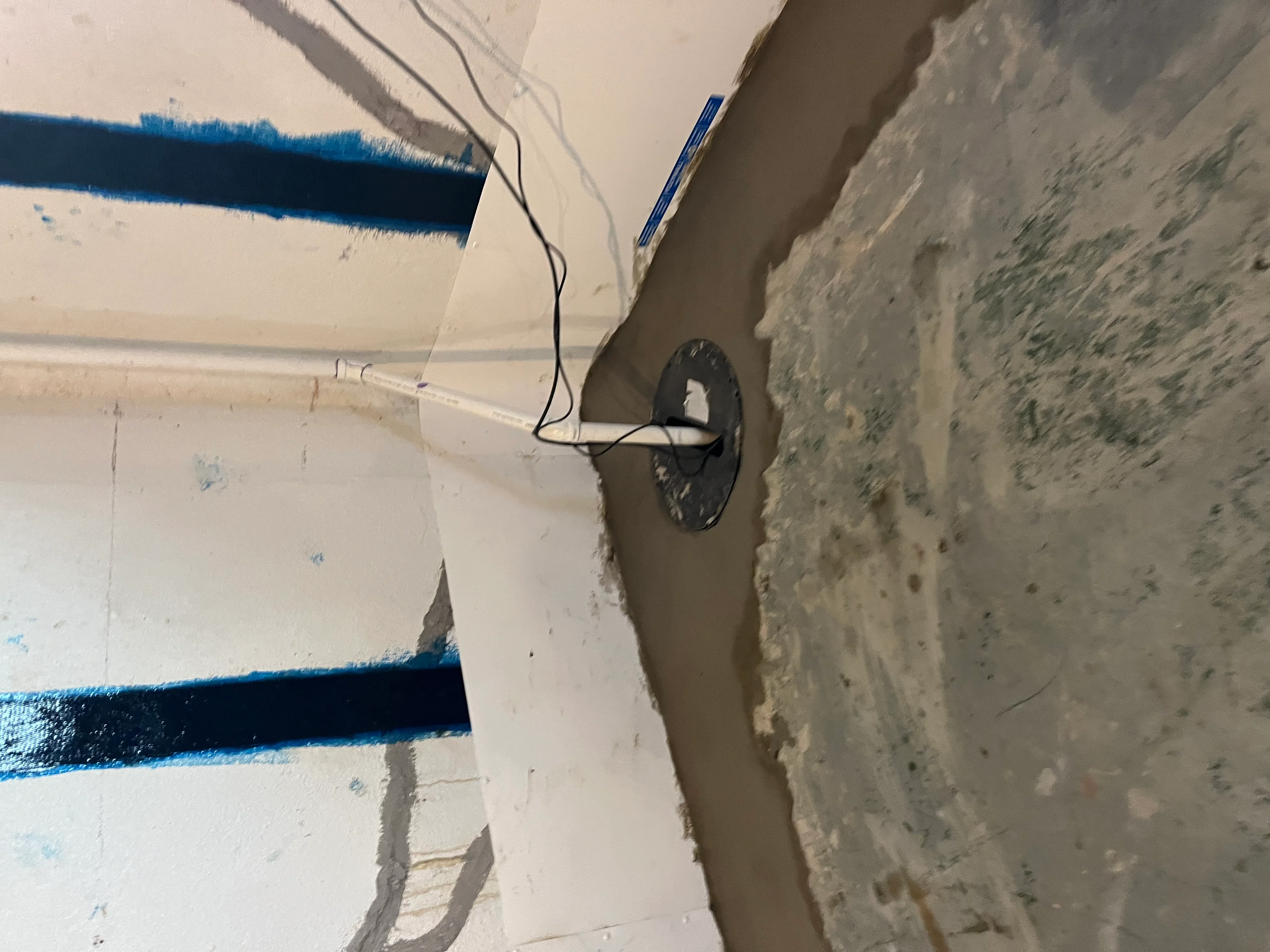 Interior waterproofing system with blue protective tape and electrical conduit on basement wall