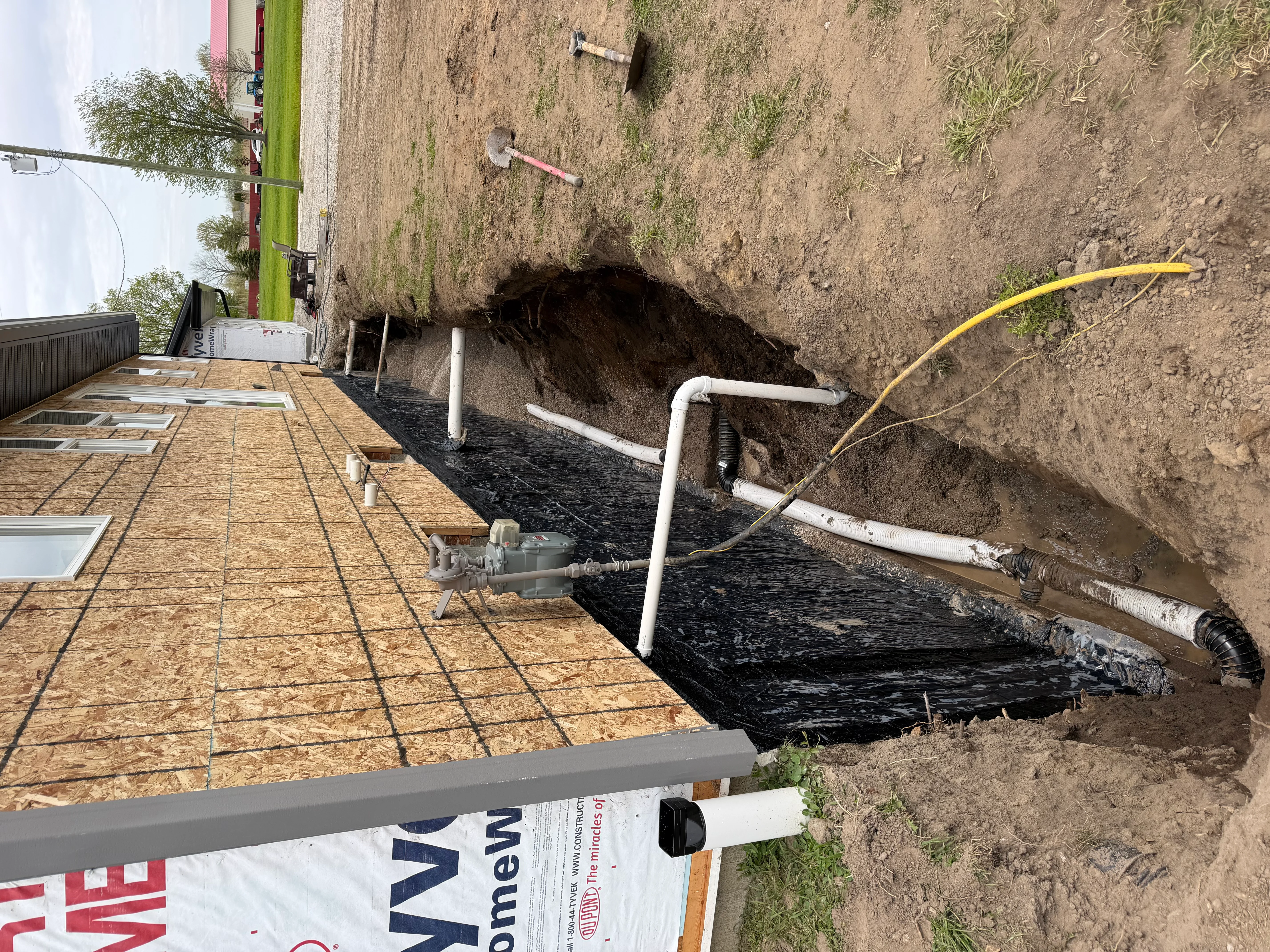 Exterior foundation waterproofing with black membrane and drainage pipes