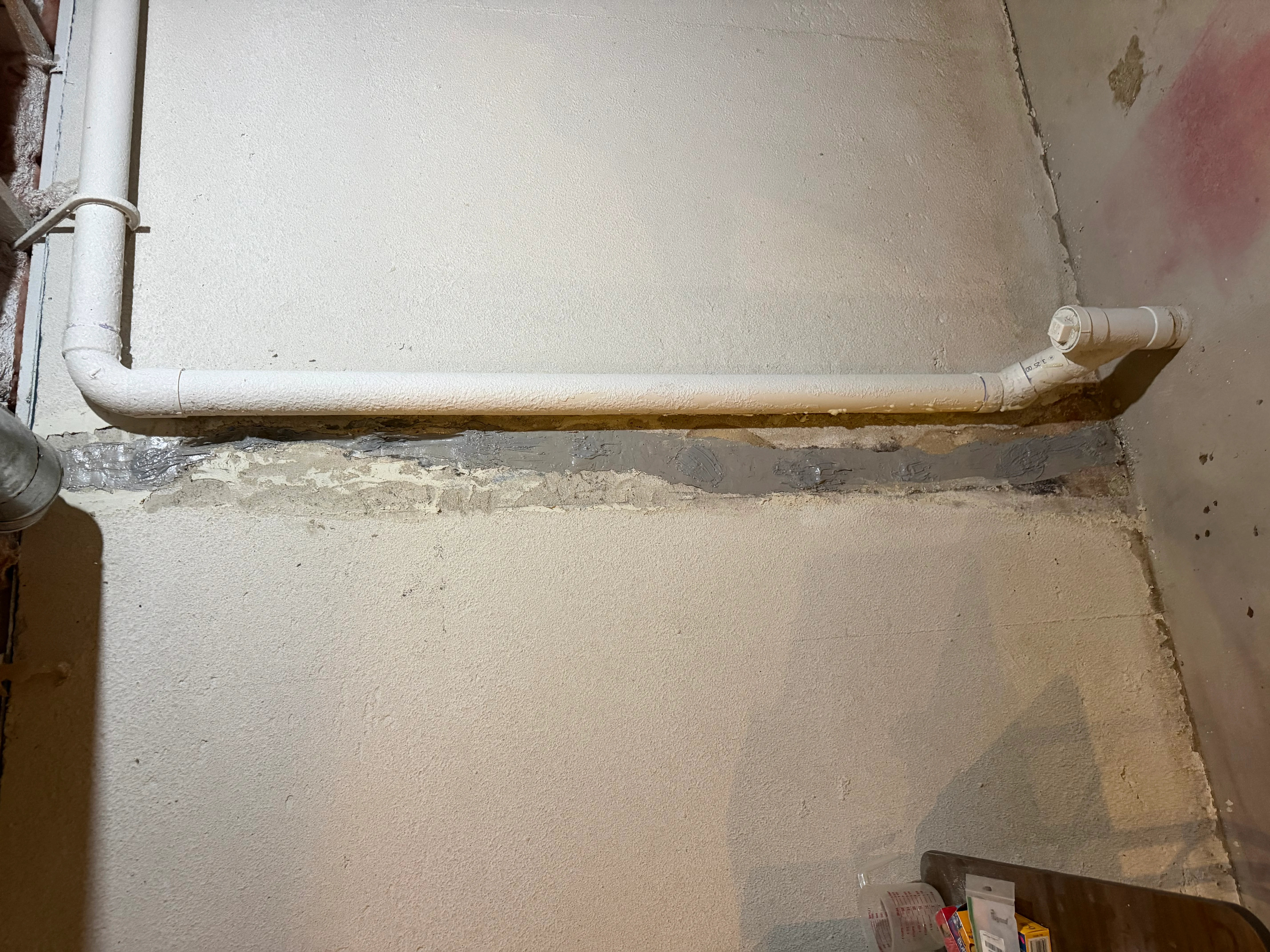 Basement wall with sealed horizontal crack and white PVC drainage pipe installed